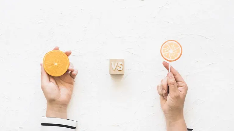 Una comparativa visual titulada "VS" que muestra una mano sosteniendo una rodaja de naranja natural frente a otra mano que sostiene un caramelo con forma de naranja, ideal para ilustrar la diferencia entre soluciones financieras saludables y opciones menos recomendables como algunos microcréditos.